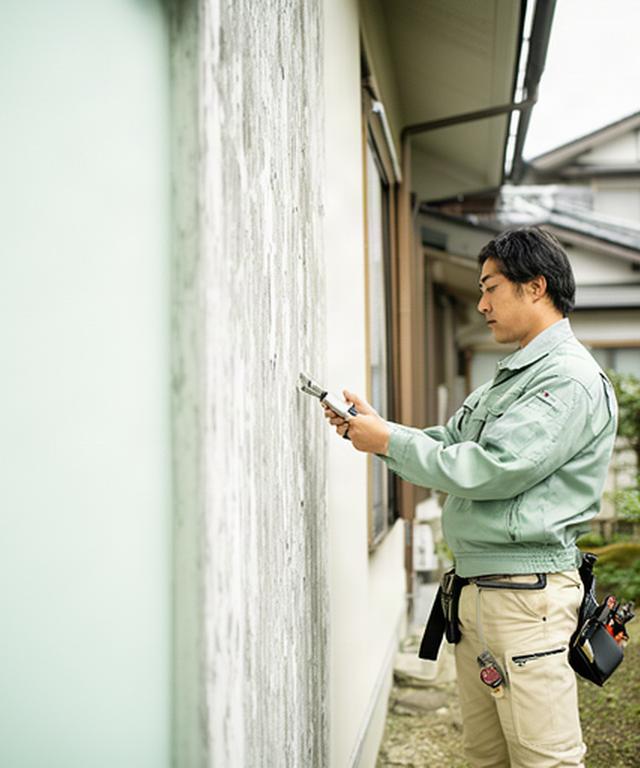 大分市の住宅を訪問し、外壁の状態を確認する住宅修理スタッフ